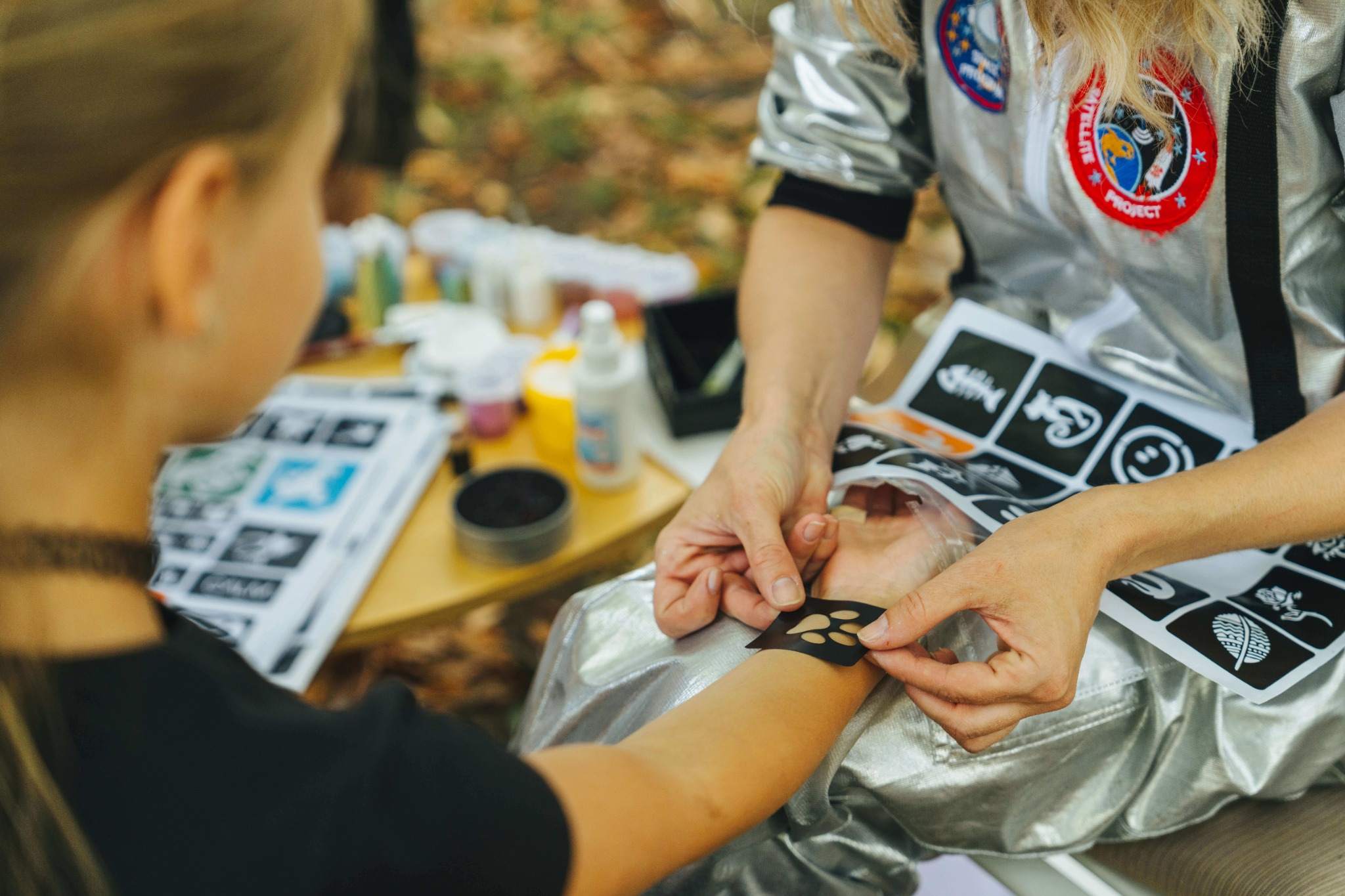 Kind gestaltet ein Glitzertattoo beim Glitter-Tattoo-Workshop